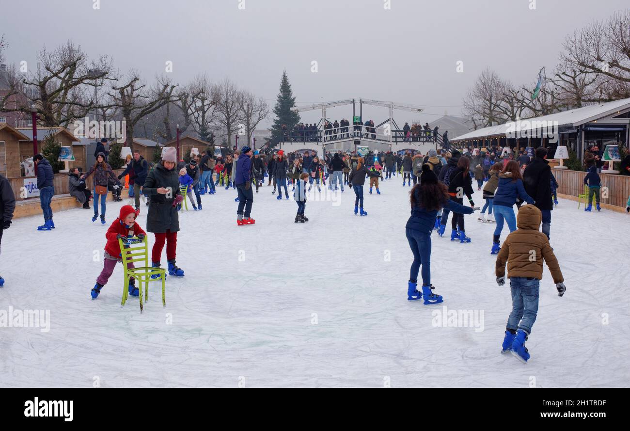 Amsterdam,Olanda-Dicembre 30,2016:Bambini e adulti che pattinano alla pista.Baby impara a pattinare con l'aiuto di una sedia.sulla piattaforma ci sono Foto Stock