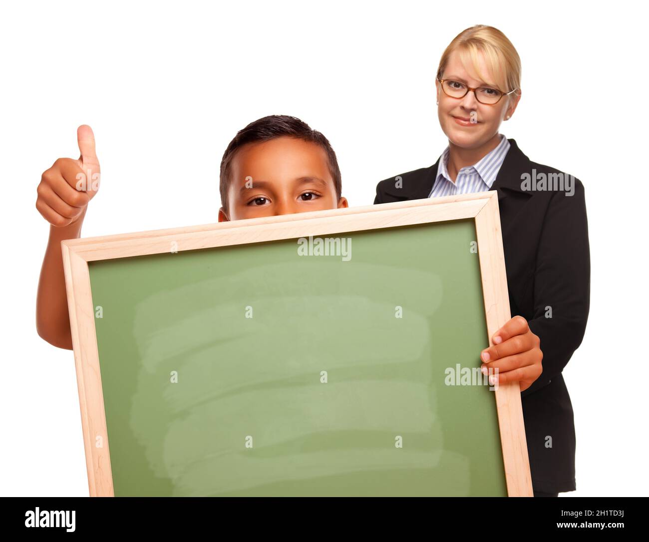 Hispanic Boy Holding Chalk Board con Thumbs Up e Female insegnante dietro isolato su uno sfondo bianco. Foto Stock