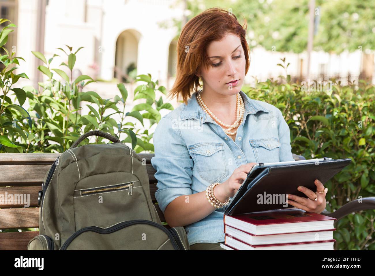 Giovane studentessa donna Pretty all'aperto con zaino e libri seduti sul banco utilizzando il tablet Touch. Foto Stock