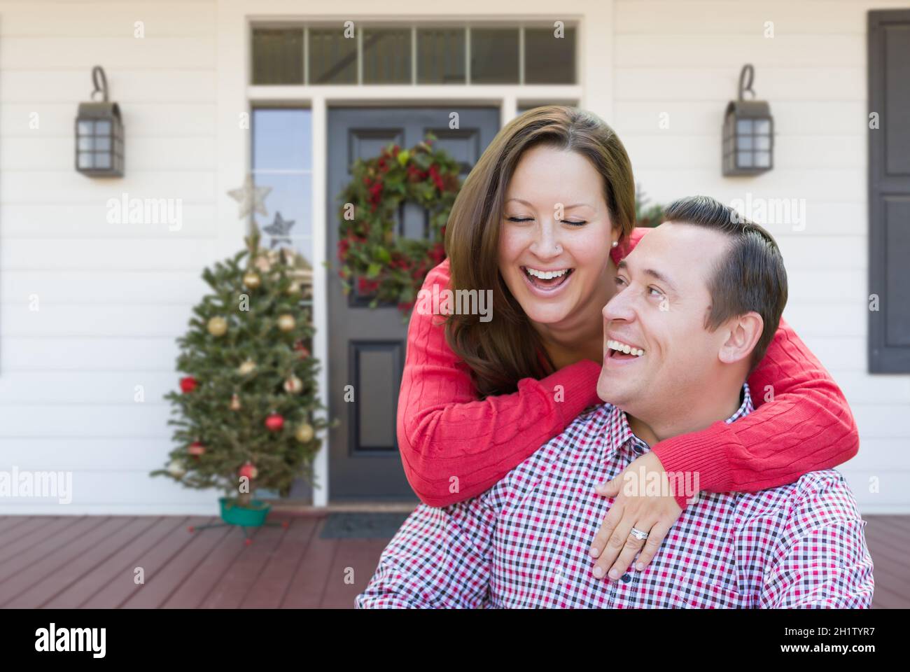 Felice Coppia Giovane ridere sul portico di casa con decorazioni di Natale. Foto Stock