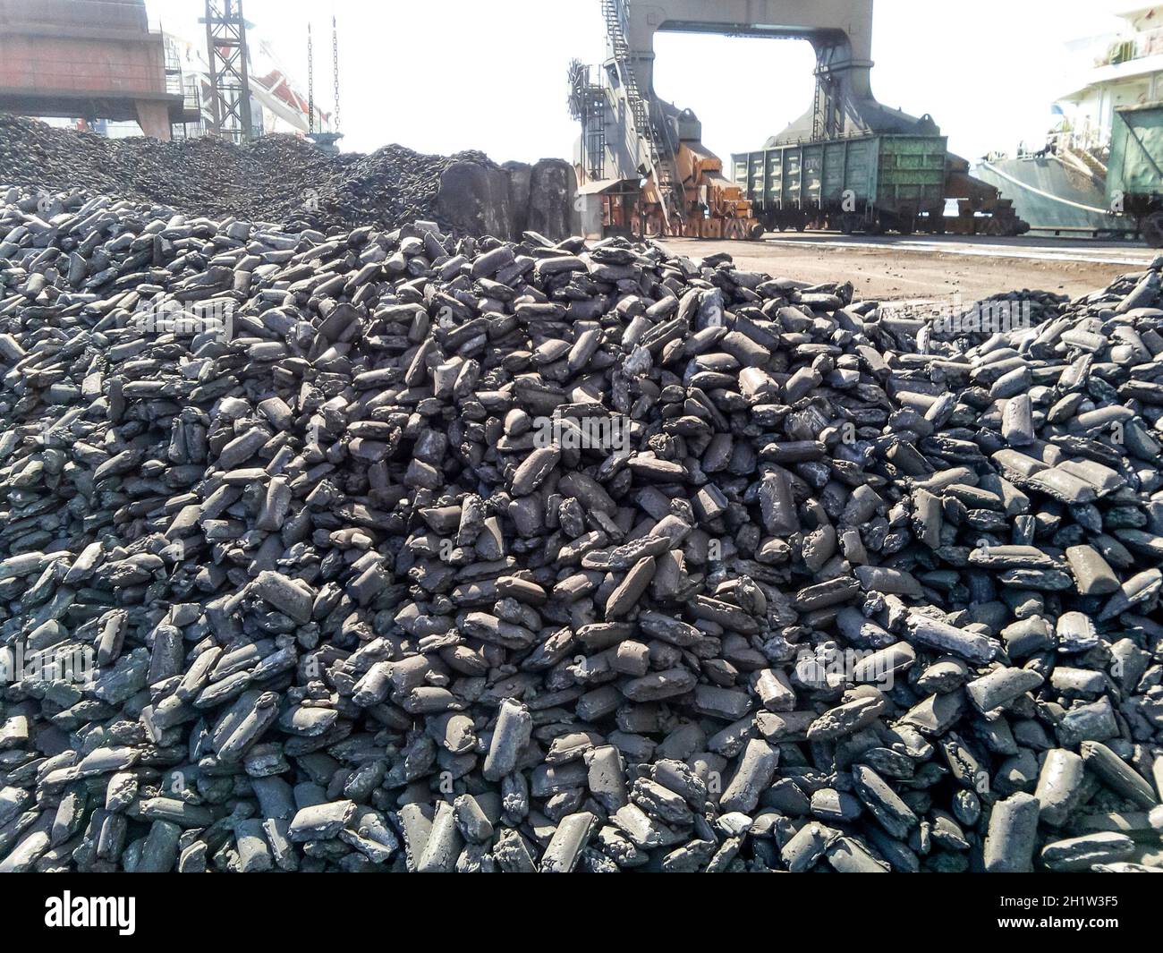 Pile di acciaio greggio bricchette. Cumulo di carbone antracite nel porto. Porto di gru per il caricamento del carbone. Foto Stock