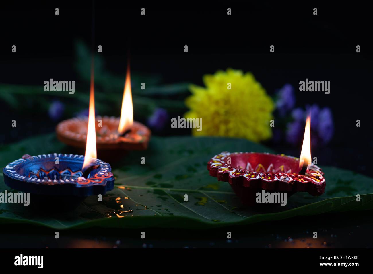 Eco-friendly artigianale colorato Clay Diya profondo o dia illuminato su foglia verde con fiori. Tema del Festival indiano per Diwali Pooja, Navratri, Duss Foto Stock