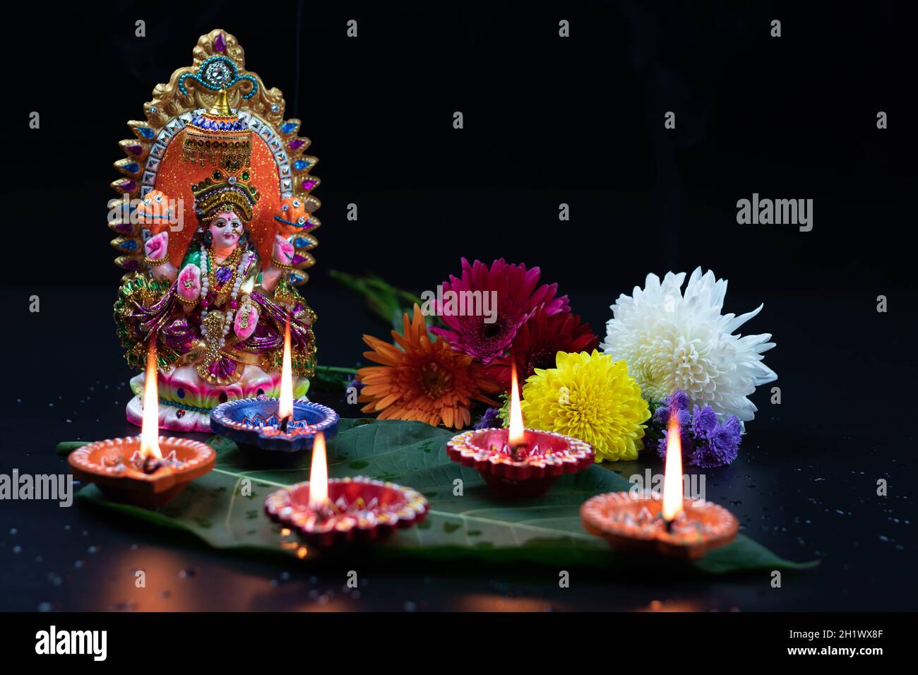Manufatti realizzati a mano Eco friendly Clay Mutti o Moorti di Hindu Mata Lashmi o Devi Laxmi Maa. Fiori decorativi e Diya Deep dia illuminato su foglia verde. Tema Fo Foto Stock