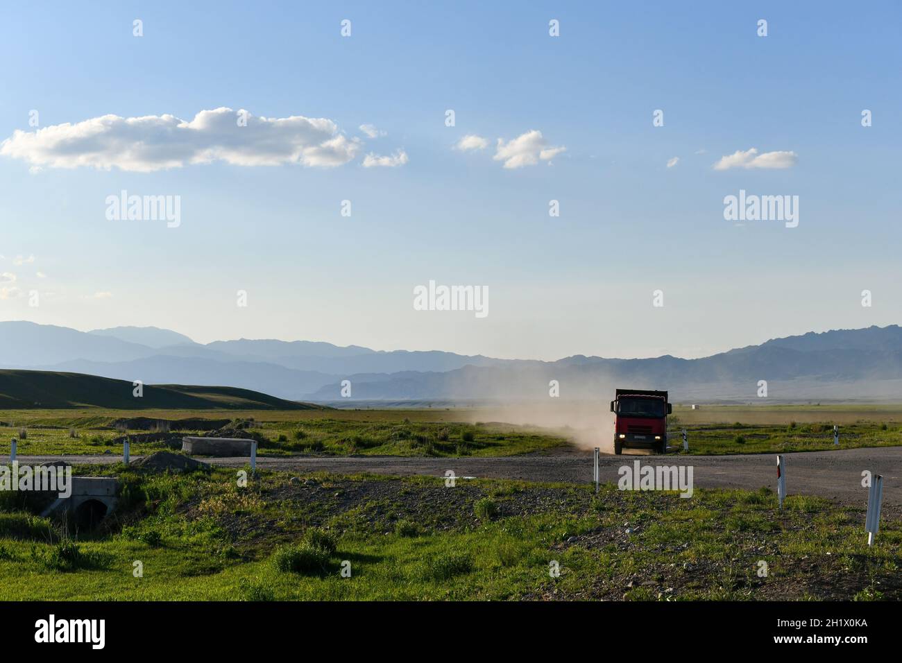 Montagne, cielo, strada, camion di carico in movimento, colonna di polvere, nuvole Foto Stock