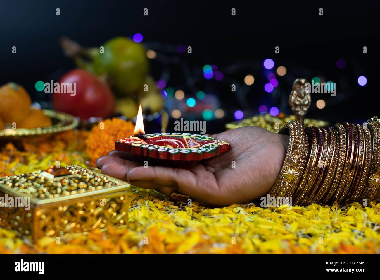 Mani di femmina Girl Holding illuminato Clay Diya profondo su Flower Bed decorazione e bokeh effetto per Diwali Puja nuovo anno Deepawali o Shubh Deepaval Foto Stock