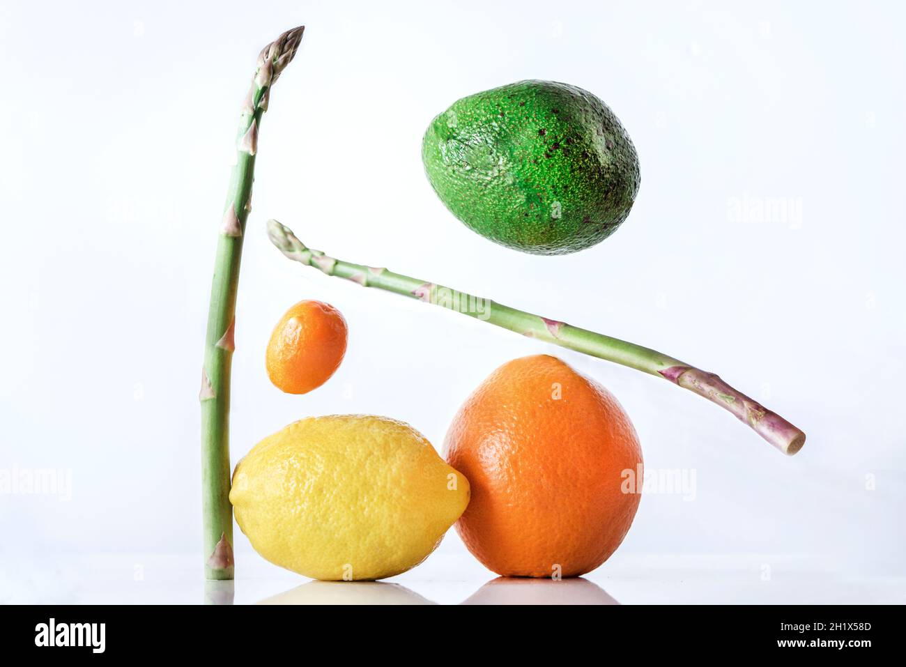Un kumquat, avocado e asparagi si levitano su sfondo bianco, primo piano, fotografia astratta Foto Stock