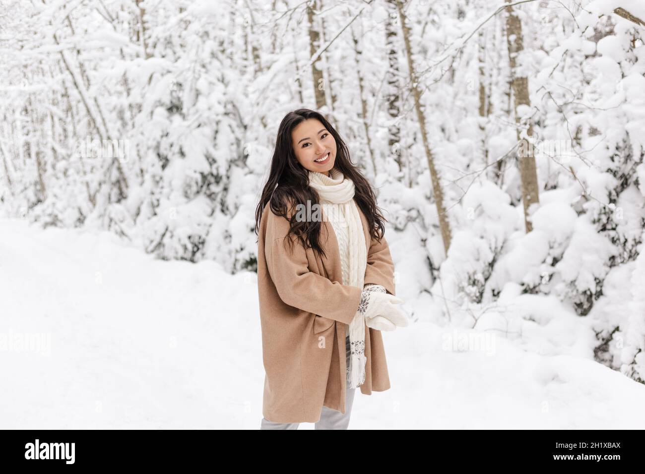 Cute Asian Girl in piedi sorridente nella foresta invernale. Inverno nevoso giorno. Bella ragazza Foto Stock