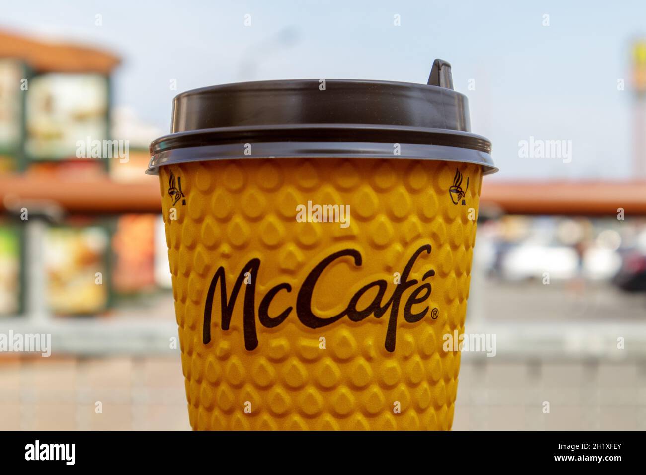 Bicchiere di vetro giallo cartaceo con caffè per bevande McCafe sul tavolo contro la città sfocata da McDonald's. Fast food di background. Fast food res Foto Stock