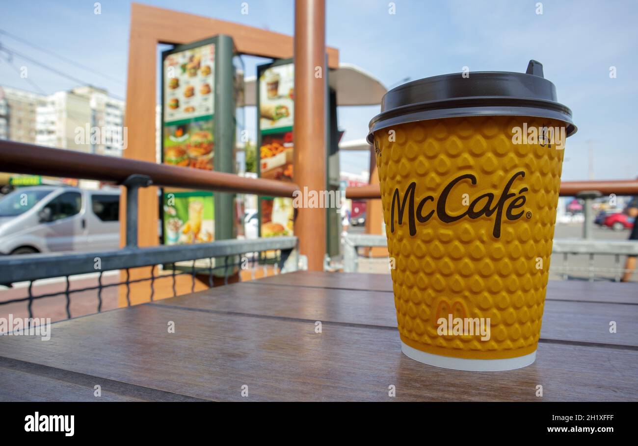 Bicchiere di vetro giallo cartaceo con caffè per bevande McCafe sul tavolo contro la città sfocata da McDonald's. Fast food di background. Fast food res Foto Stock