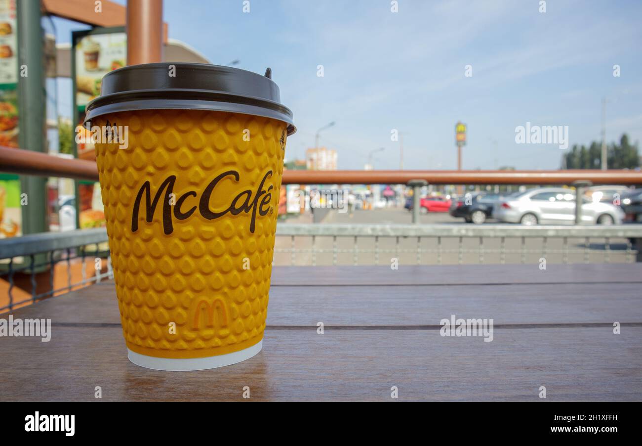 Bicchiere di vetro giallo cartaceo con caffè per bevande McCafe sul tavolo contro la città sfocata da McDonald's. Fast food di background. Fast food res Foto Stock