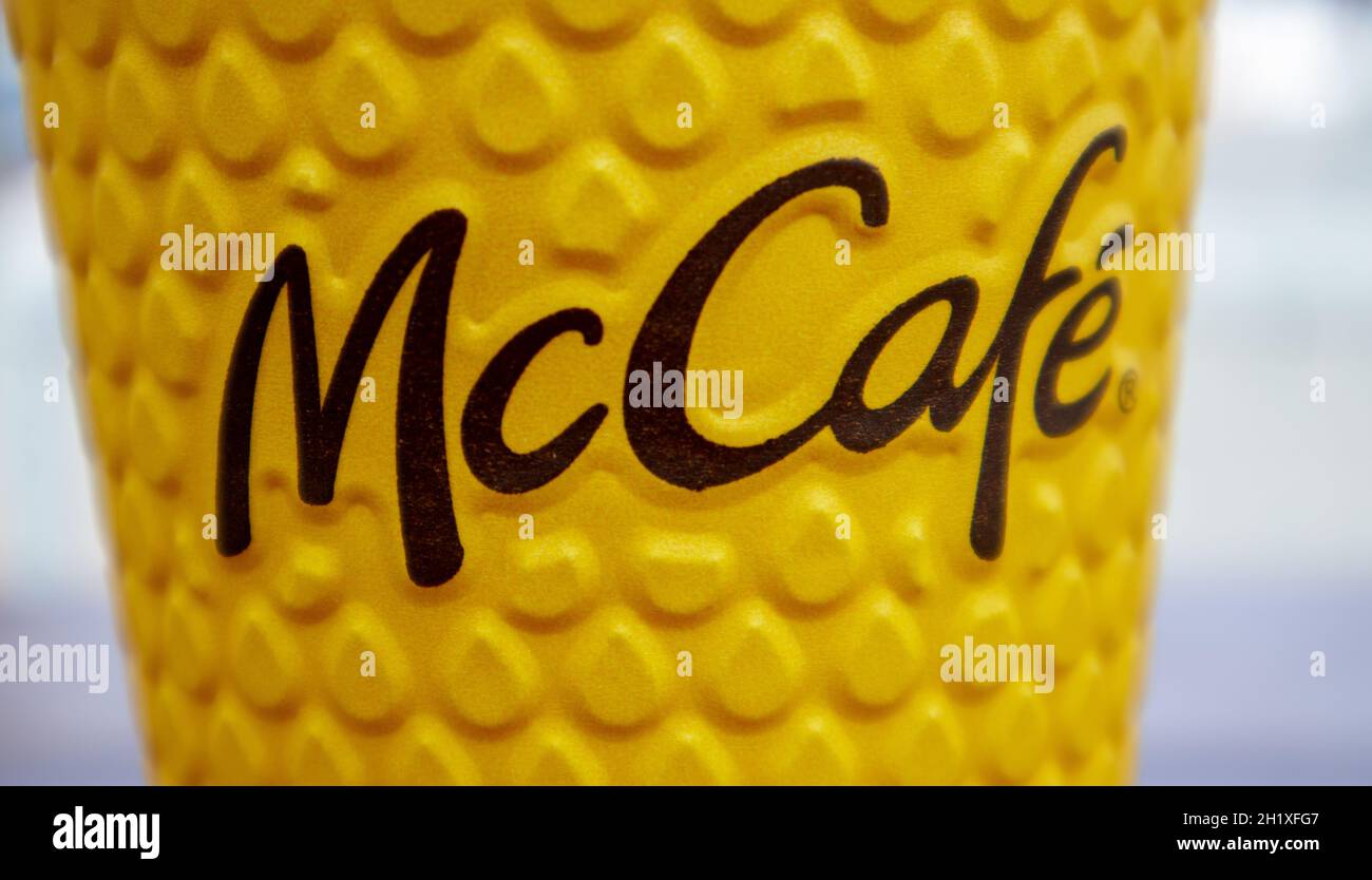 Bicchiere di vetro giallo cartaceo con caffè per bevande McCafe sul tavolo contro la città sfocata da McDonald's. Fast food di background. Fast food res Foto Stock