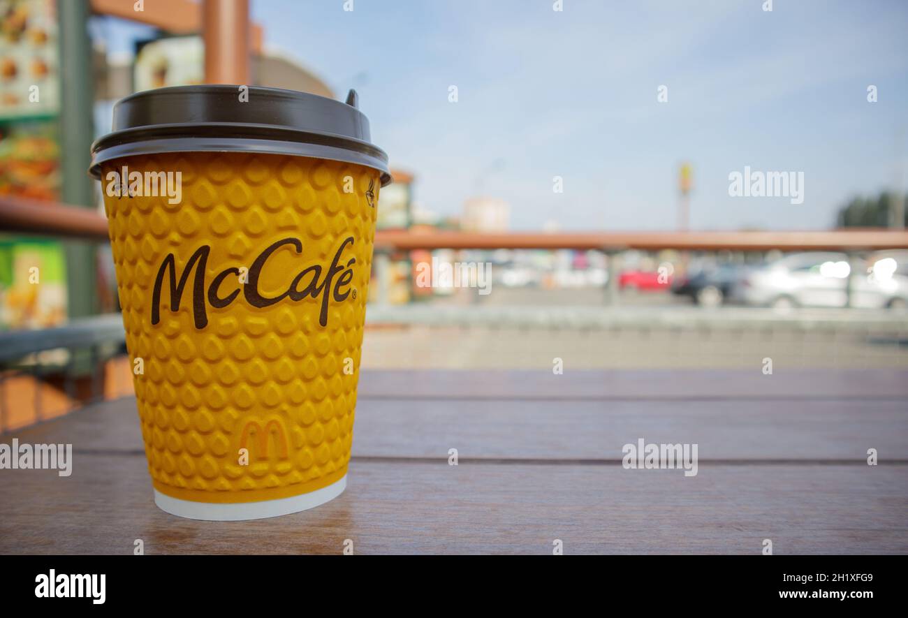 Bicchiere di vetro giallo cartaceo con caffè per bevande McCafe sul tavolo contro la città sfocata da McDonald's. Fast food di background. Fast food res Foto Stock