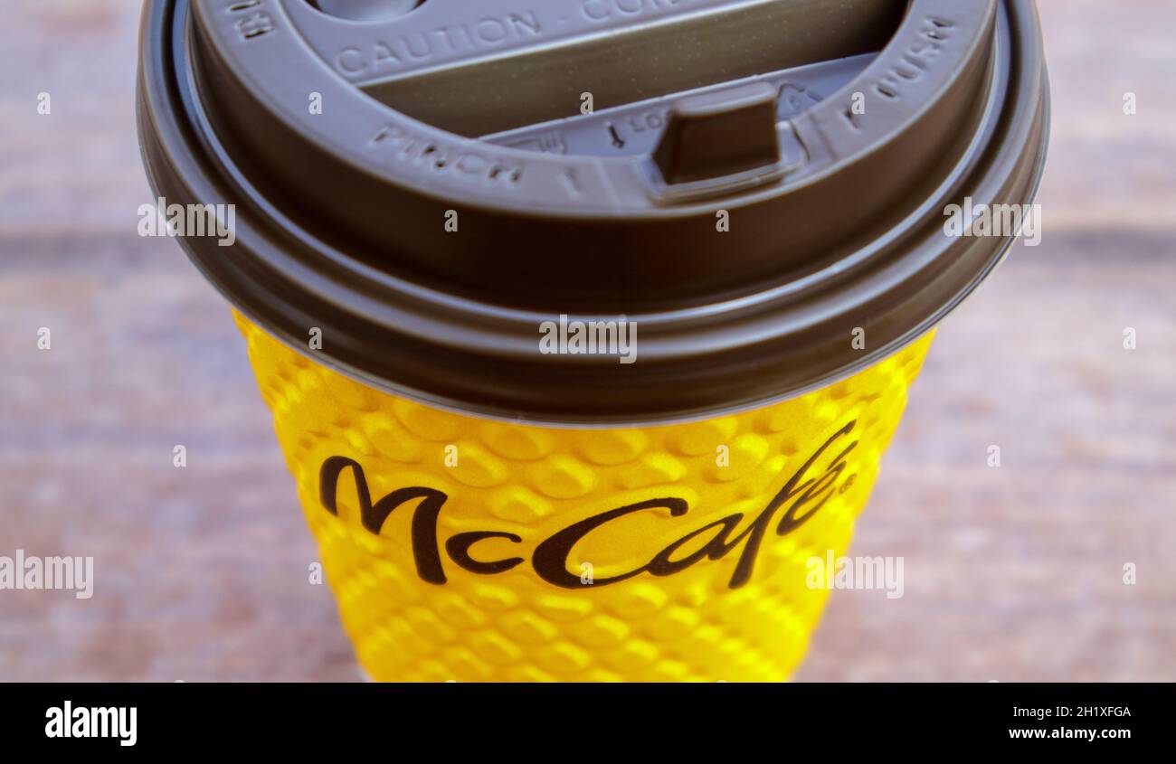 Bicchiere di vetro giallo cartaceo con caffè per bevande McCafe sul tavolo contro la città sfocata da McDonald's. Fast food di background. Fast food res Foto Stock