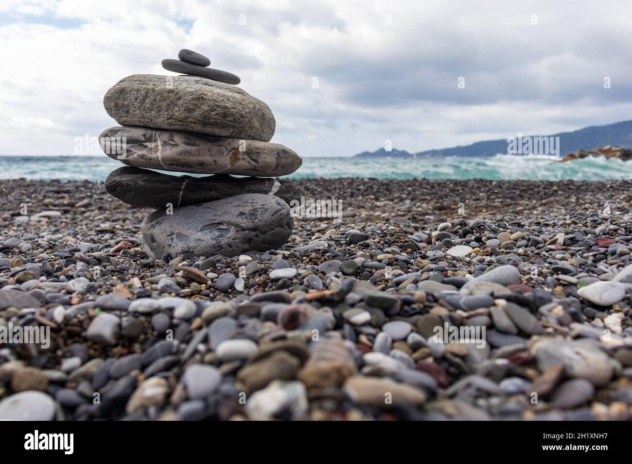 Piramide delle pietre sulla spiaggia contro il mare ruvido. Sul backgorund il promontorio di Portofino (Italia). Concetto di spiritualità, relax, zen. Foto Stock