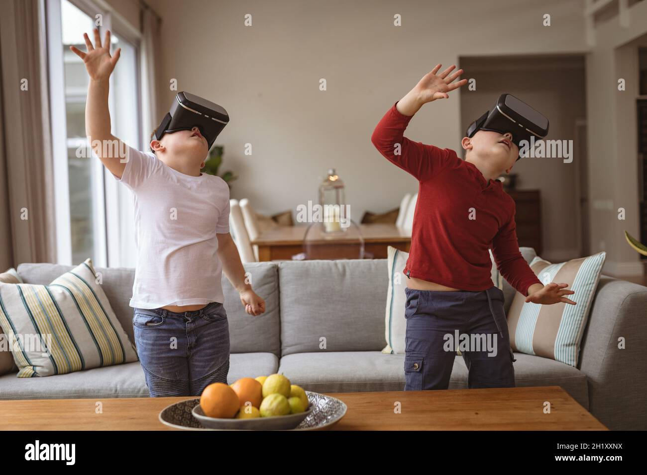 Due ragazzi caucasici che indossano cuffie per realtà virtuale che gesturano nel salotto di casa Foto Stock