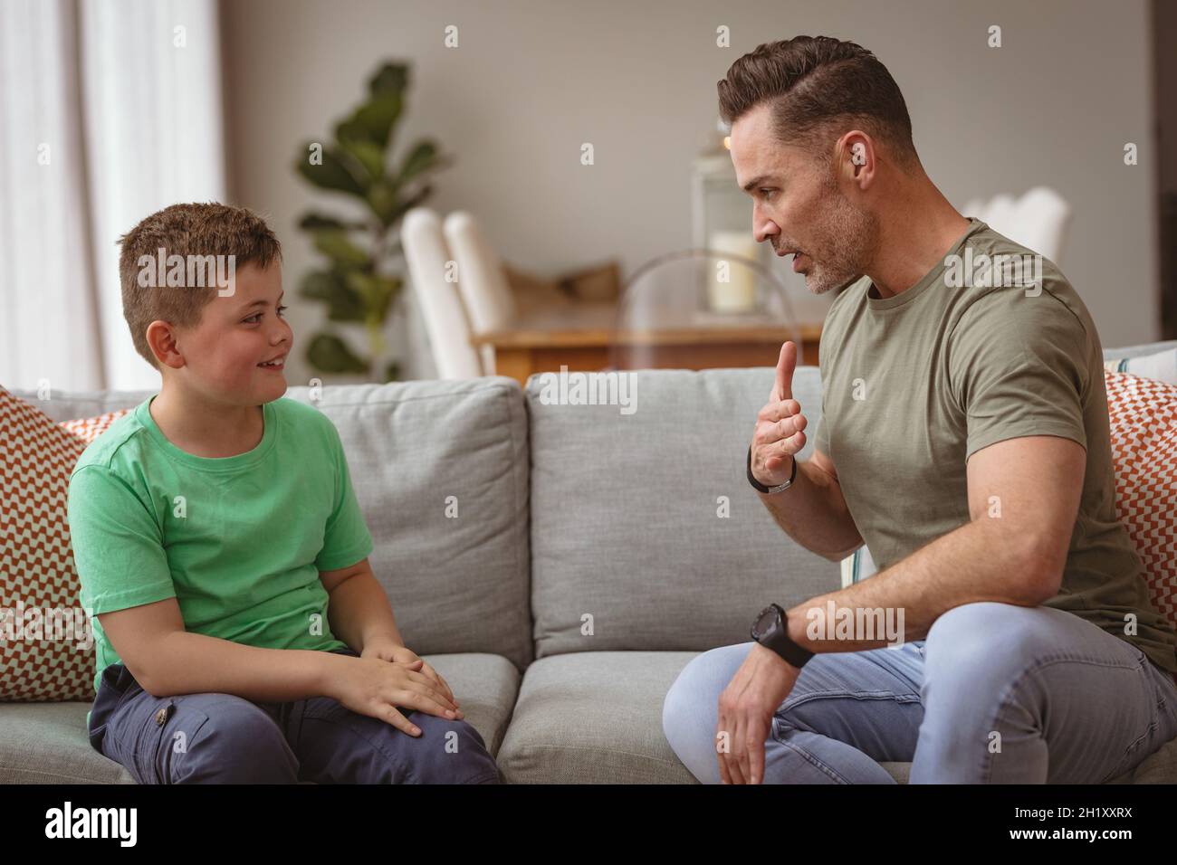 Padre e figlio caucasici che comunicano utilizzando il linguaggio dei segni mentre si siede sul divano a casa Foto Stock