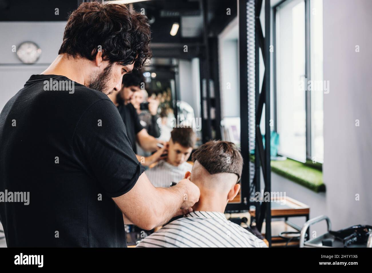 Bello alto barbiere bearded bruna dà un haircut trendy ad un adolescente. Riflessione nello specchio. Taglio professionale e styling per uomo in un barbe Foto Stock