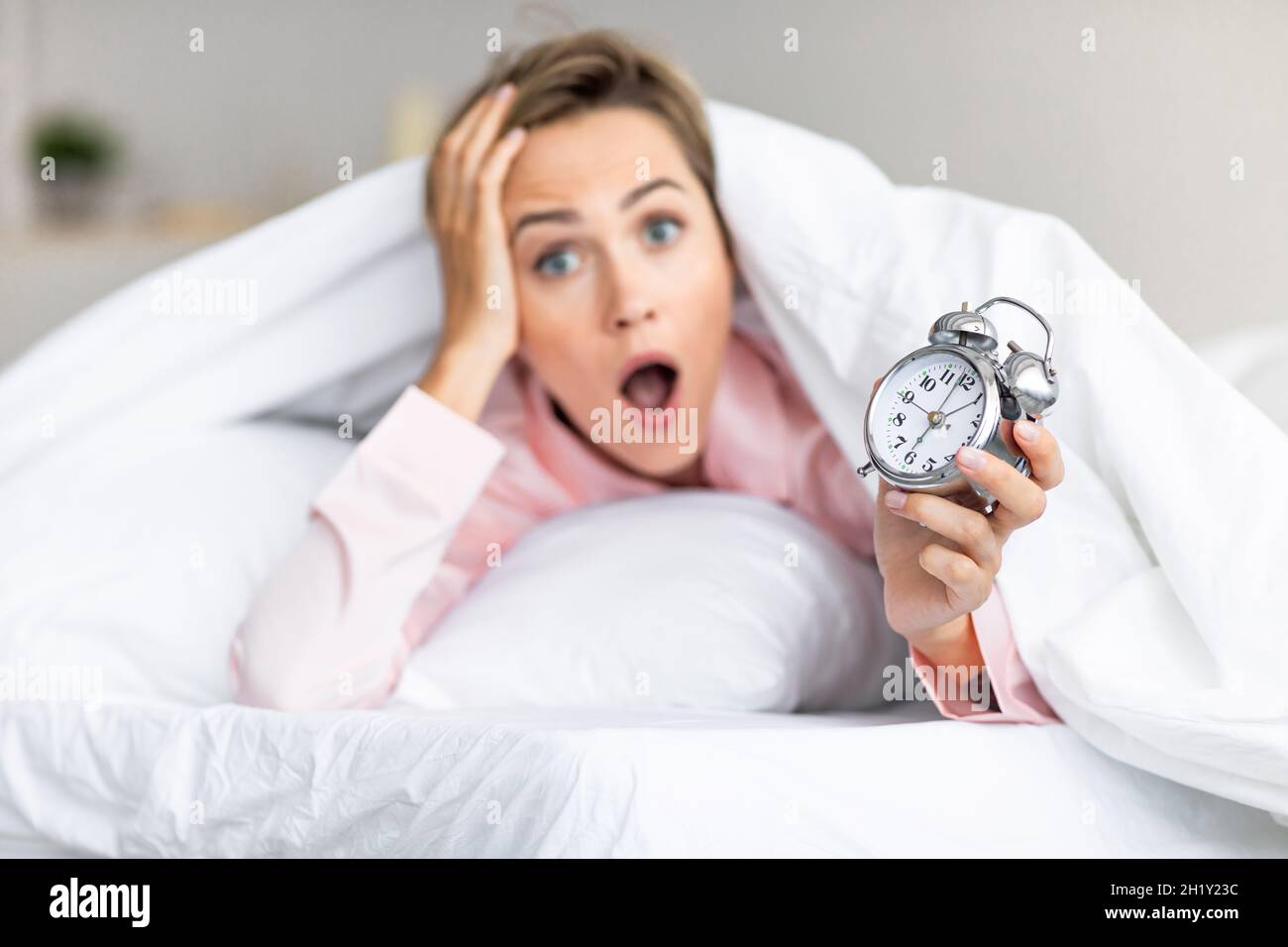 Segnale acustico eccessivo. Ritratto di donna scioccata che tiene l'orologio a letto Foto Stock
