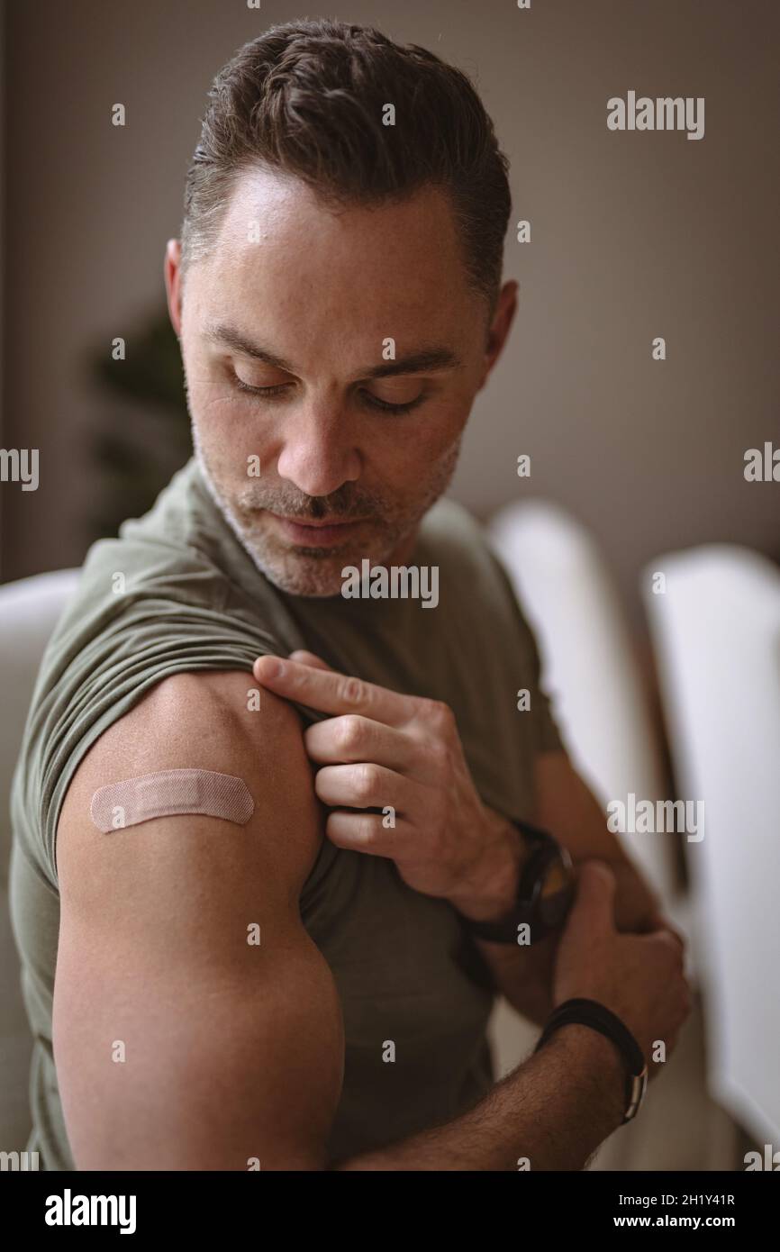 Uomo caucasico che mostra la spalla vaccinata a casa Foto Stock