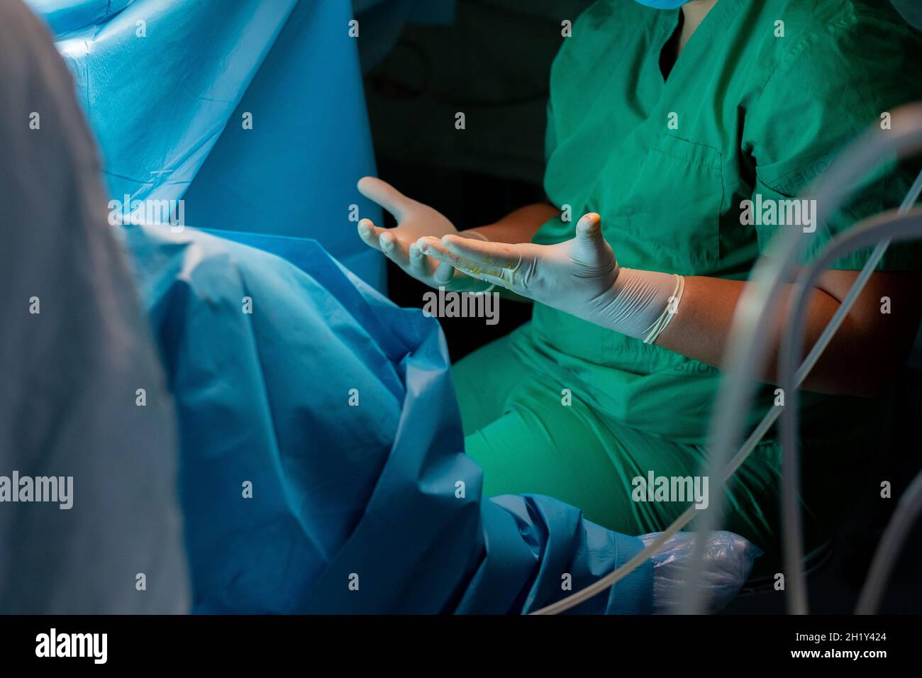 Mani del chirurgo in guanti sterili in lattice. Un chirurgo in uniforme verde tira in avanti le dita sparse in guanti chirurgici sterili. Le mani del chirurgo durante l'intervento chirurgico. Foto Stock