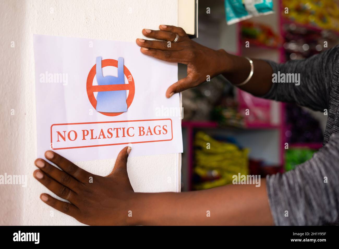 primo piano dell'irriconoscibile negoziante che incolla nessun avviso di sacchetto di plastica sulla parete - concetto per ridurre la poluzione e l'uso di plastica nei negozi al dettaglio. Foto Stock