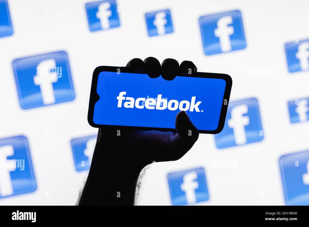 Smartphone con il logo del social network di Facebook sullo schermo in una mano applaiata sullo sfondo dei logo di Facebook Foto Stock