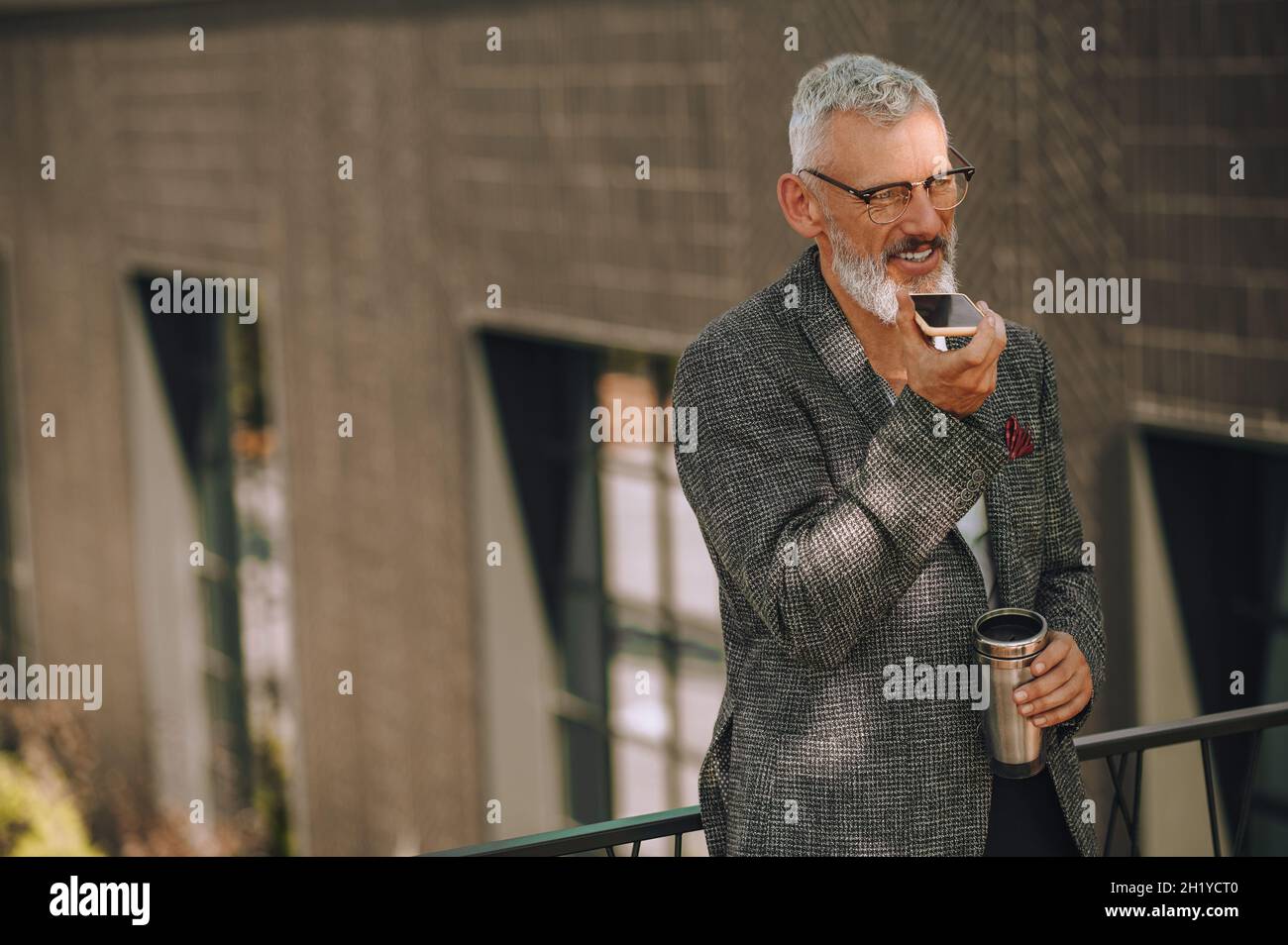 Un uomo dai capelli grigi negli occhiali che registra un messaggio audio Foto Stock