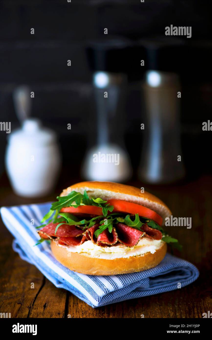 Un bagel con formaggio cremoso, salame al pepe, razzo e pomodori Foto Stock