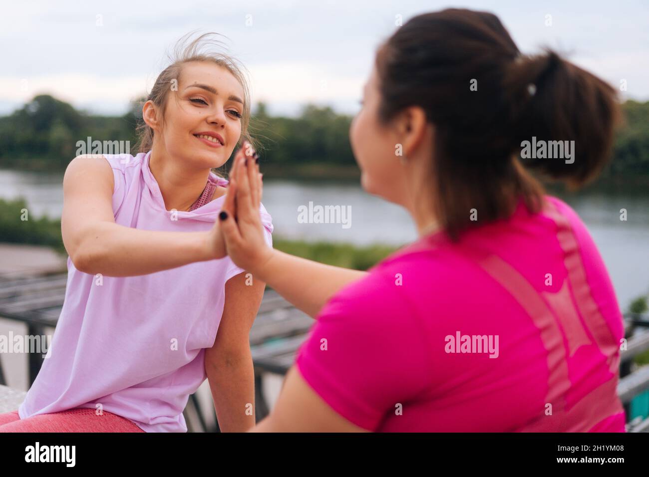 Primo piano-up back view di fitness positivo femmina trainer e motivato grasso giovane donna che si salutano a vicenda con alto-cinque altri dopo l'esercizio all'aperto Foto Stock