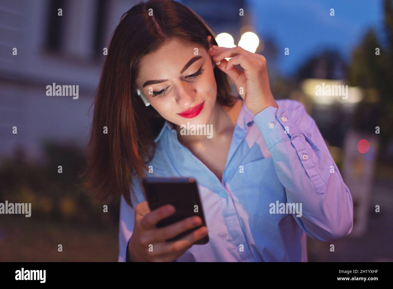 La giovane donna caucasica ha indossato la cuffia wireless di notte in città Foto Stock