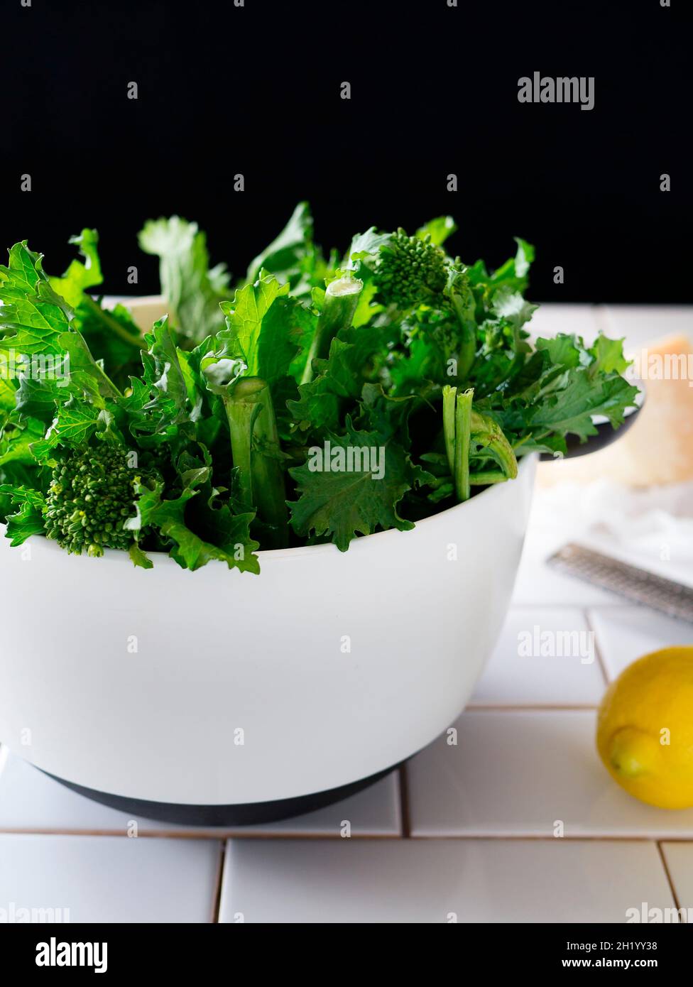 Broccolini in una ciotola bianca, con un limone e un blocco di parmigiano Foto Stock