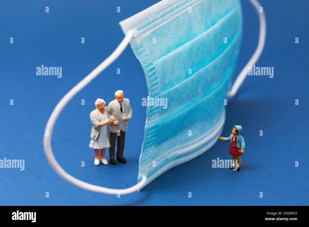 Maschera medica e persone su sfondo blu, concetto sul tema della distanza sociale, uomini giocattolo di plastica Foto Stock