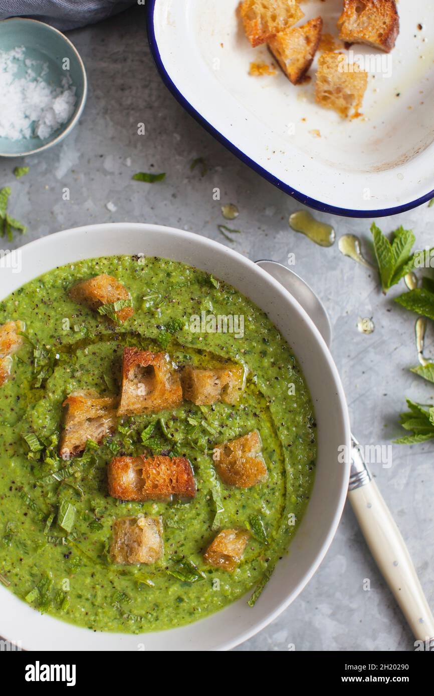 Zuppa estiva di piselli, asparagi e crescione ricoperta di crostini di pasta madre, olio extra vergine di oliva e menta fresca Foto Stock