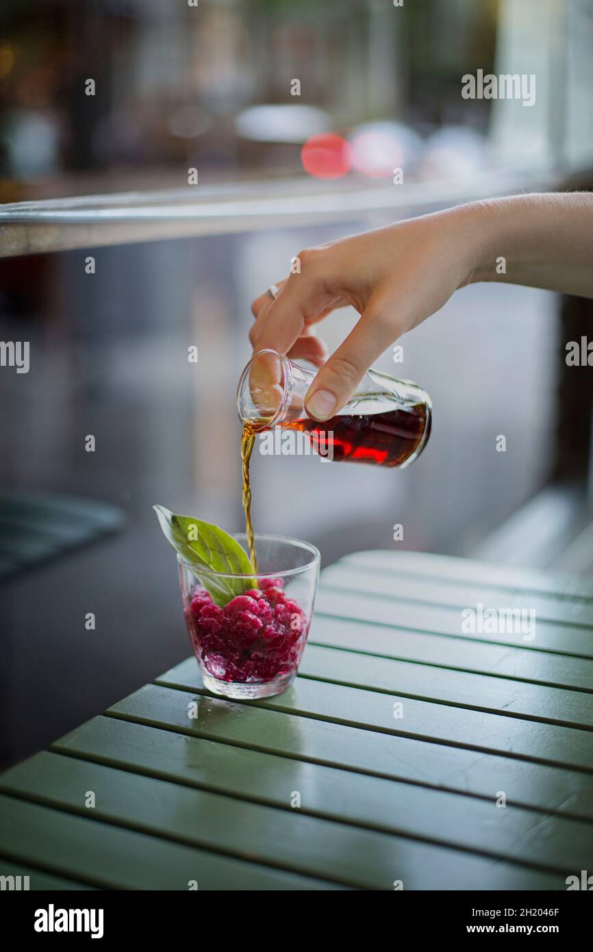 Un lato di versamento di liquore alle erbe su melograno granita in un bicchiere Foto Stock