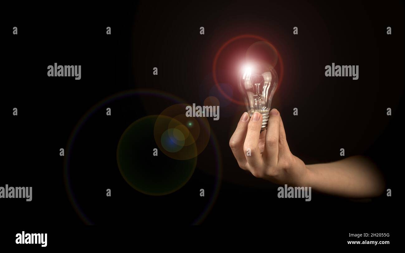 Mano di donna che tiene la lampadina illuminata su sfondo nero. Idea, innovazione, pensiero e ispirazione per il concetto aziendale Foto Stock