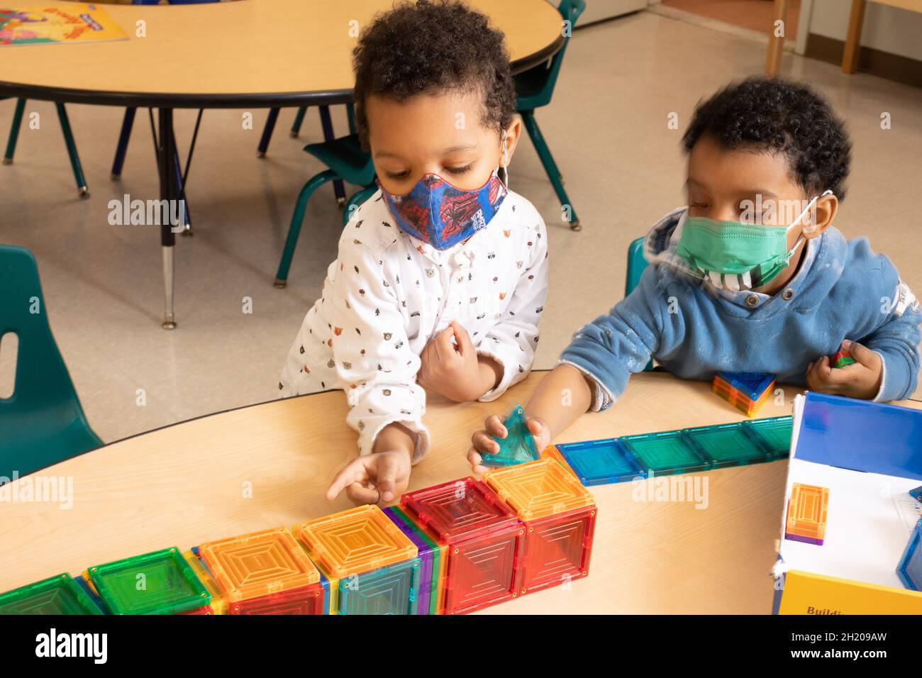 Istruzione Preschool 3-4 anni due ragazzi costruendo con piastrelle magnetiche, un ragazzo contando e puntando a pezzi, entrambi ragazzi indossando maschere per proteggere aga Foto Stock