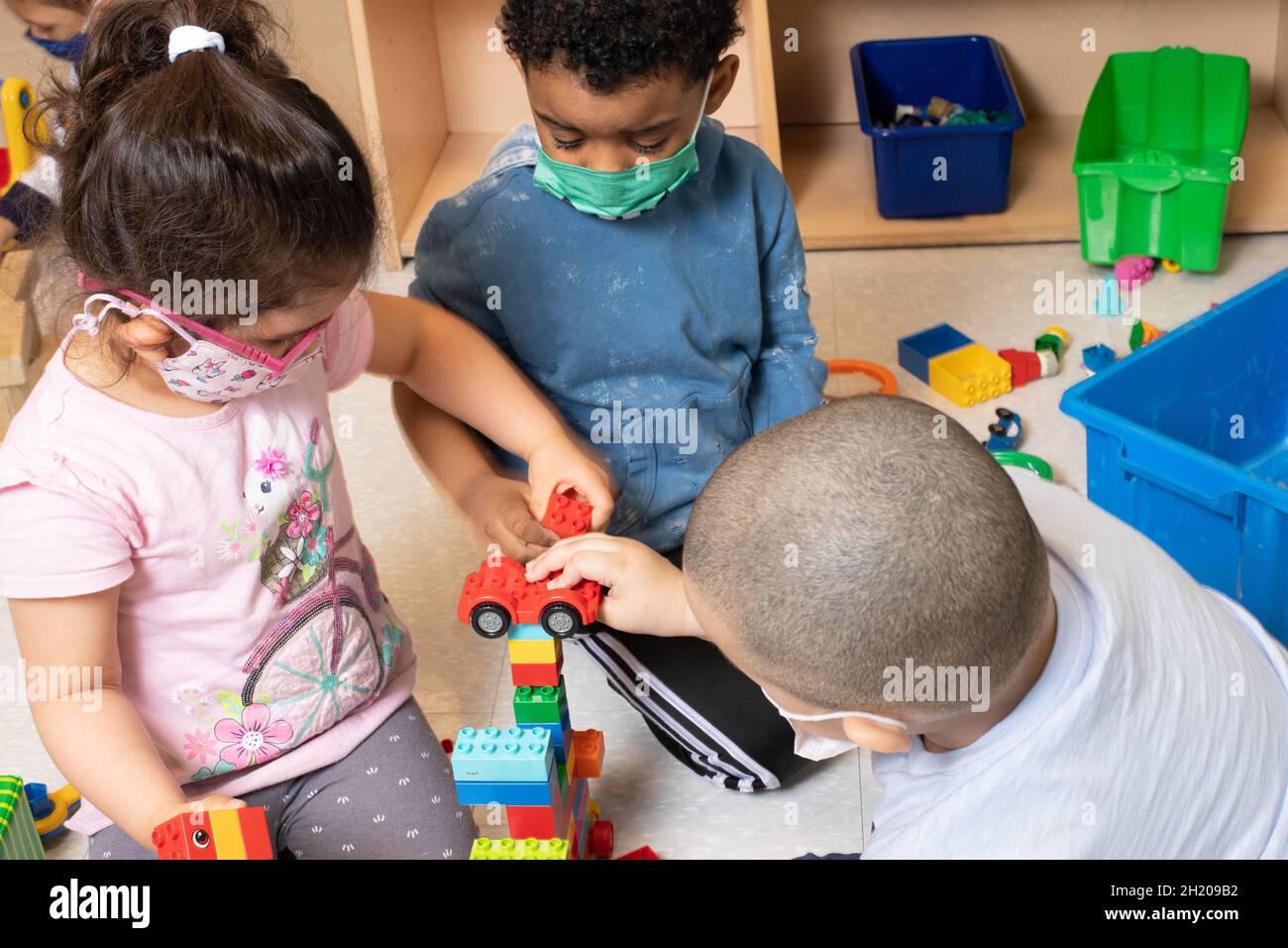 Istruzione Preschool 3-4 anni due ragazzi e una ragazza che giocano nell'area a blocchi con veicoli giocattolo e una costruzione che hanno costruito da coloratissimo collegamento b Foto Stock