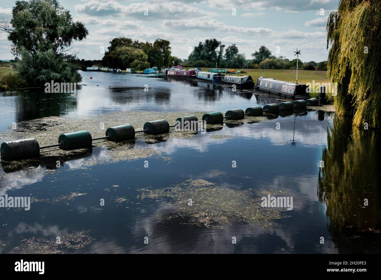 Botisham lucchetto chiusa e sbarramento barriera di protezione sul fiume Cam con barche a remi ormeggiate sulla riva del fiume in Cambridgeshire Inghilterra Foto Stock