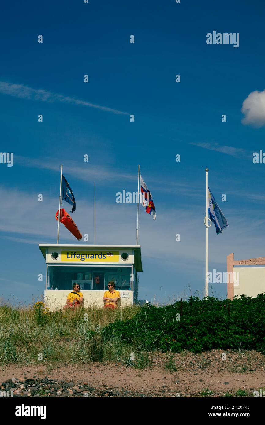 Due bagnini RNLI presso la stazione di bagnino sulla spiaggia Leven Fife Scotland UK con bandiere e calzini a vento Foto Stock