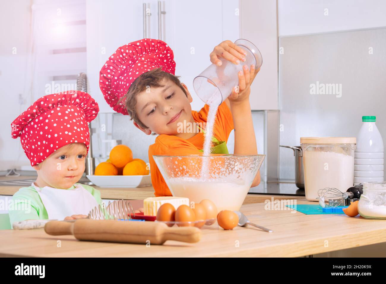 I ragazzi che cucinano nel cappello dello chef aggiungono lo zucchero al recipiente di miscelazione Foto Stock