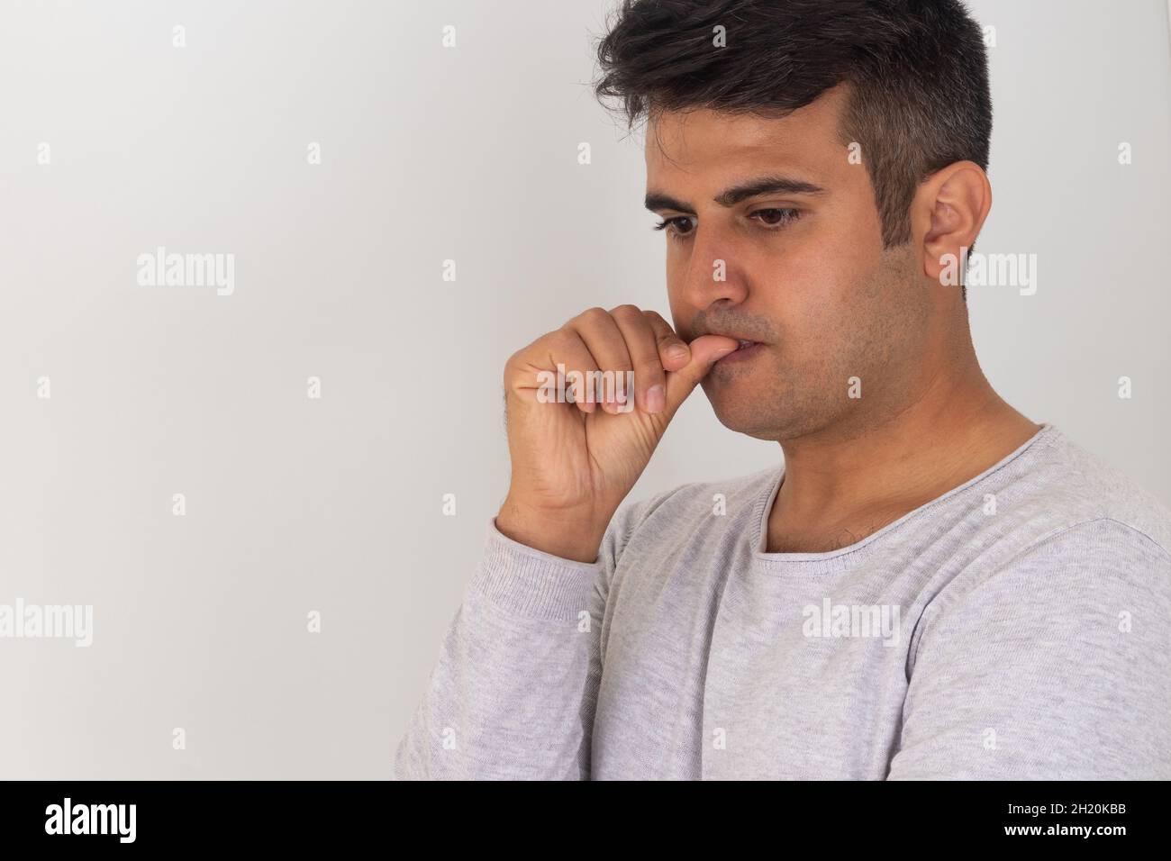 L'uomo stressato morde le unghie delle dita su sfondo isolato. Foto Stock