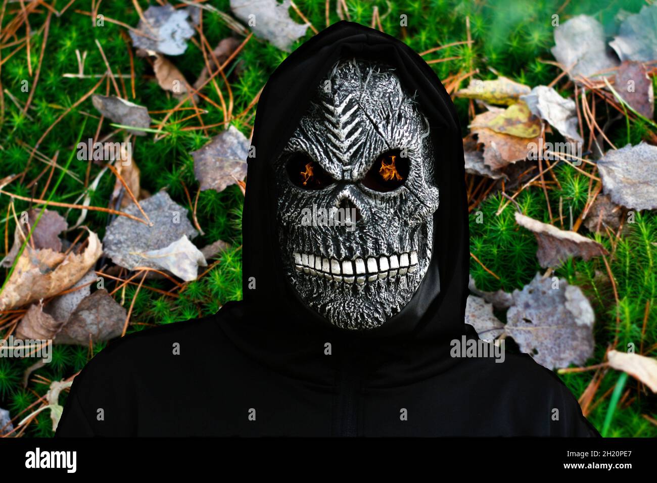 Primo piano ritratto di graniglia Reaper. Uomo in maschera di morte con fuoco fiamma negli occhi sulla natura verde muschio e secco foglie sfondo. Costume di Carnevale Foto Stock