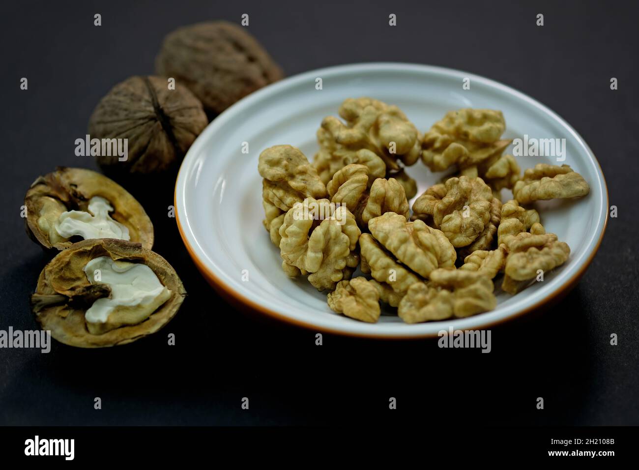 Vista dall'alto chicchi di noce. Noci sbucciate e in guscio su fondo nero. Noci marroni, intere. Noccioli di noce in un piatto. Foto Stock