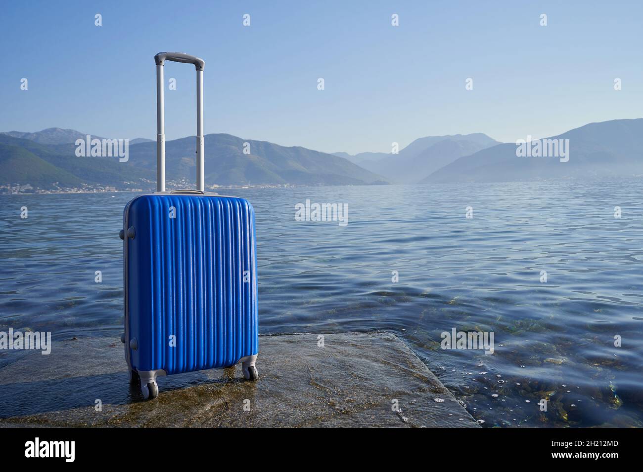 Valigia blu sullo sfondo del mare e delle montagne. Foto Stock