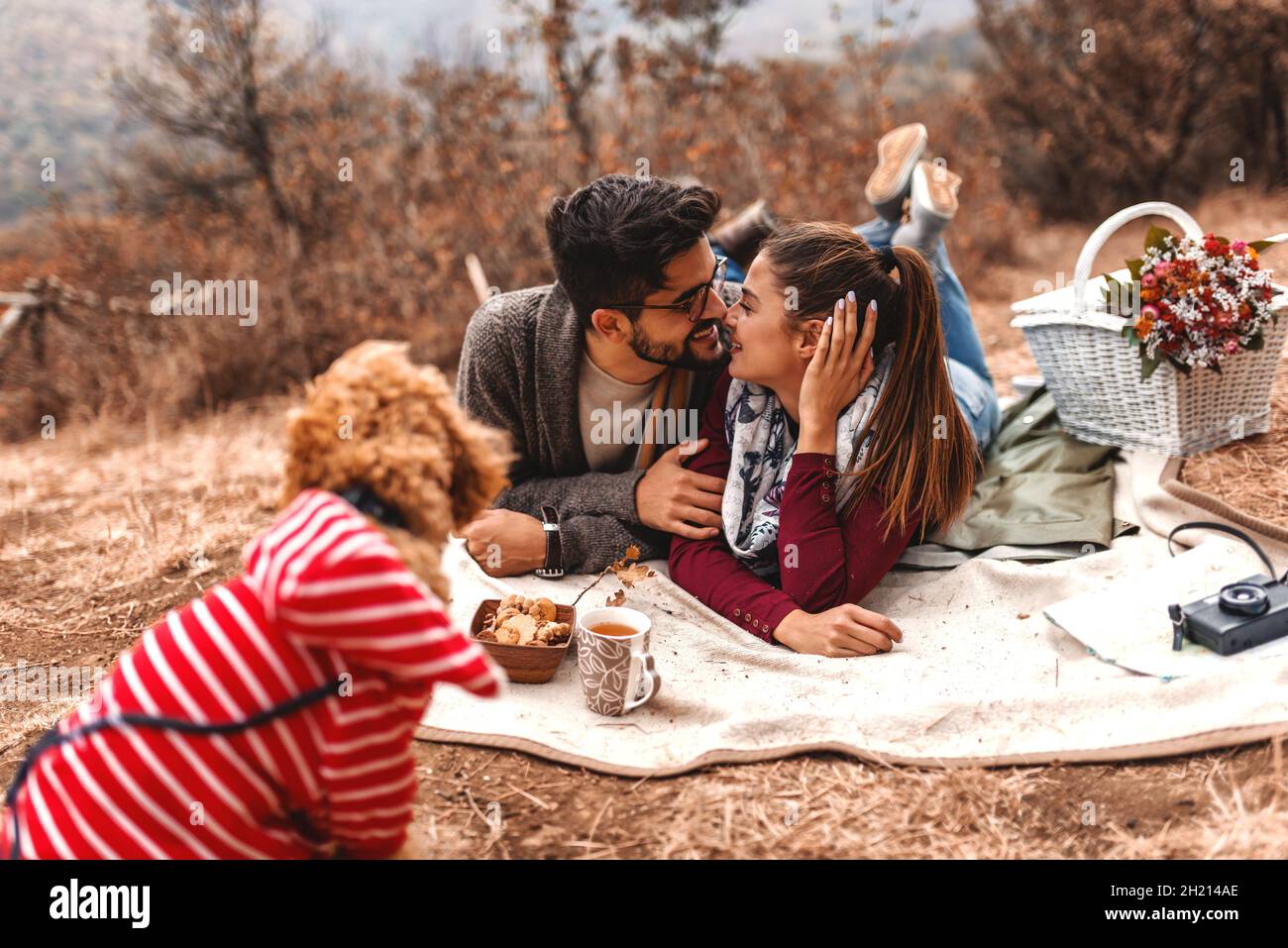 Coppia al pic-nic sdraiati su coperta e baciare. Cane che li guarda. Attenzione selettiva alla coppia. Ora di autunno. Foto Stock