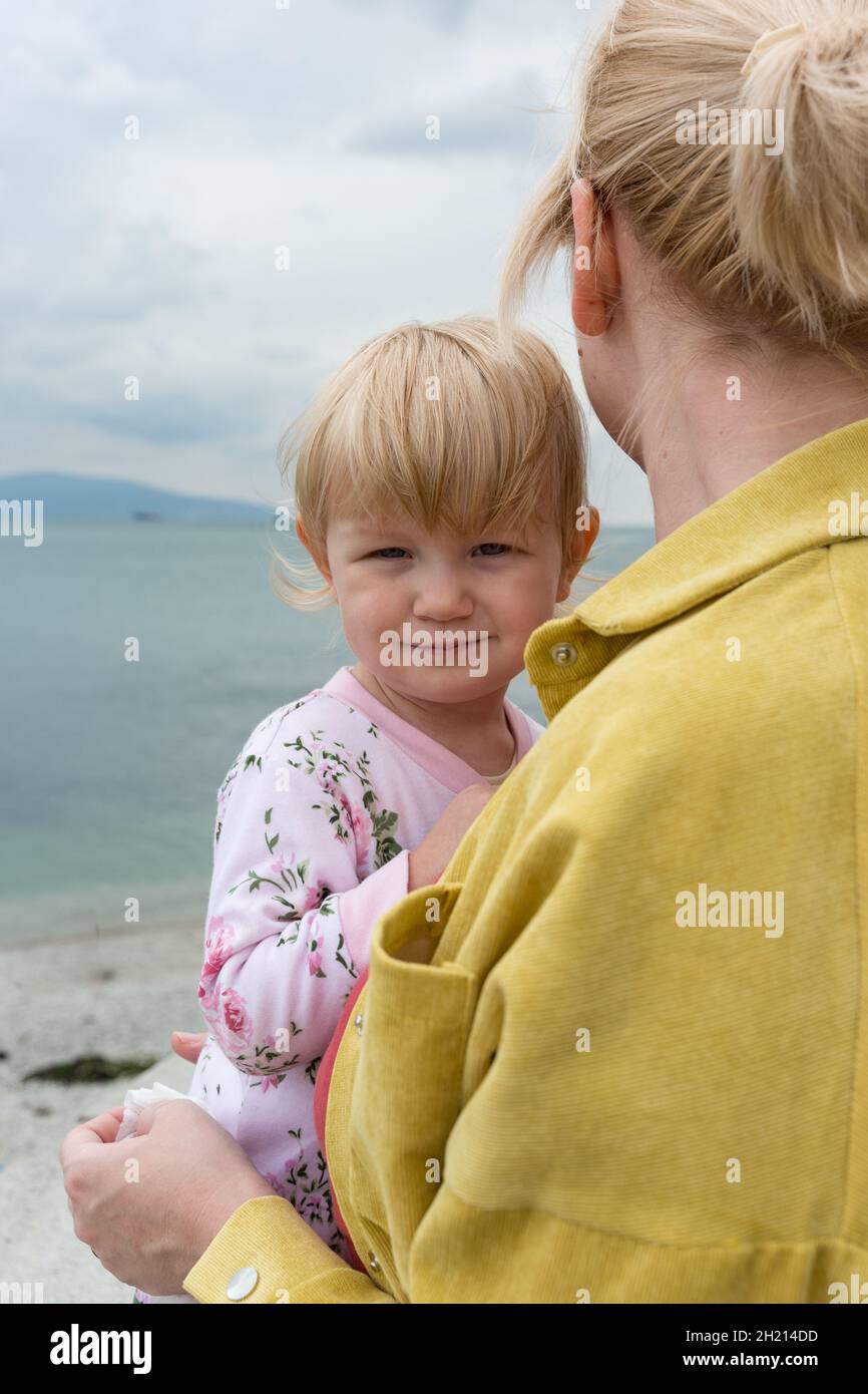 Una bambina fra le braccia di sua madre. Una donna con un bambino si alza sulla riva del mare e guarda in lontananza Foto Stock