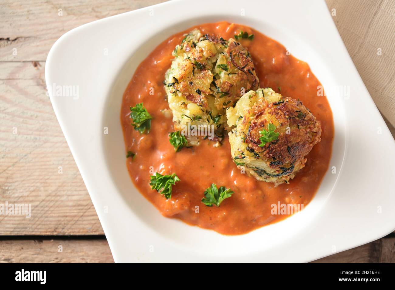 Palle di verdure di zucchine e patate in salsa di pomodoro con prezzemolo guarnire in un moderno piatto bianco su un rustico tavolo di legno, vegano e vegetariano A. Foto Stock