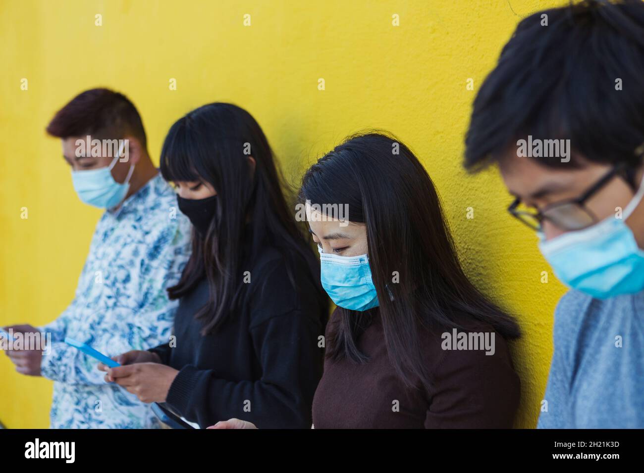 Gruppo di persone asiatiche che utilizzano il telefono cellulare mentre indossano la maschera facciale Foto Stock