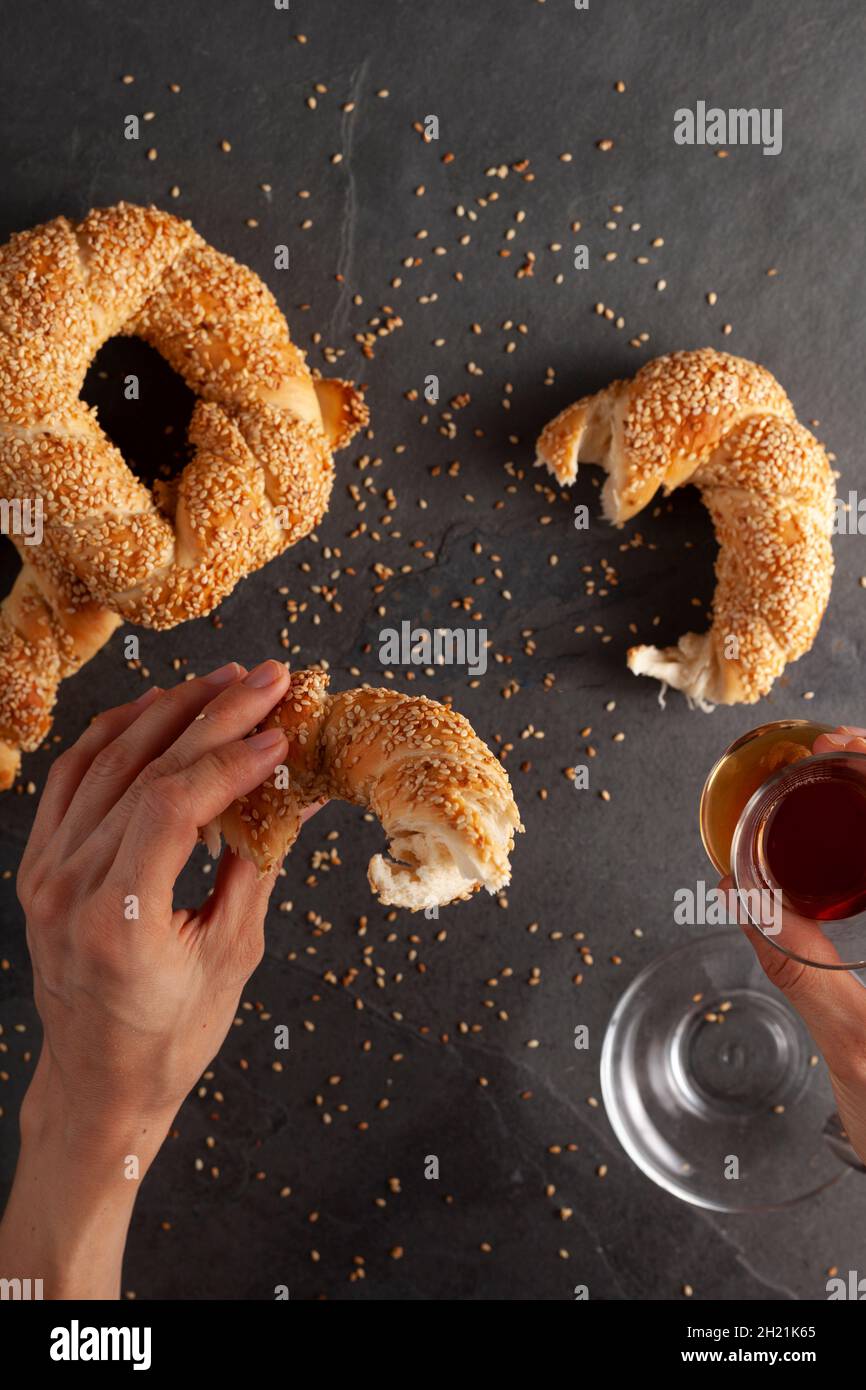 Delizioso bagel turco con semi di sesamo noti come susamli simit. Una donna sta mangiando un pezzo del bagel e tenendo una tazza di tè nero in mano. Piatto Foto Stock