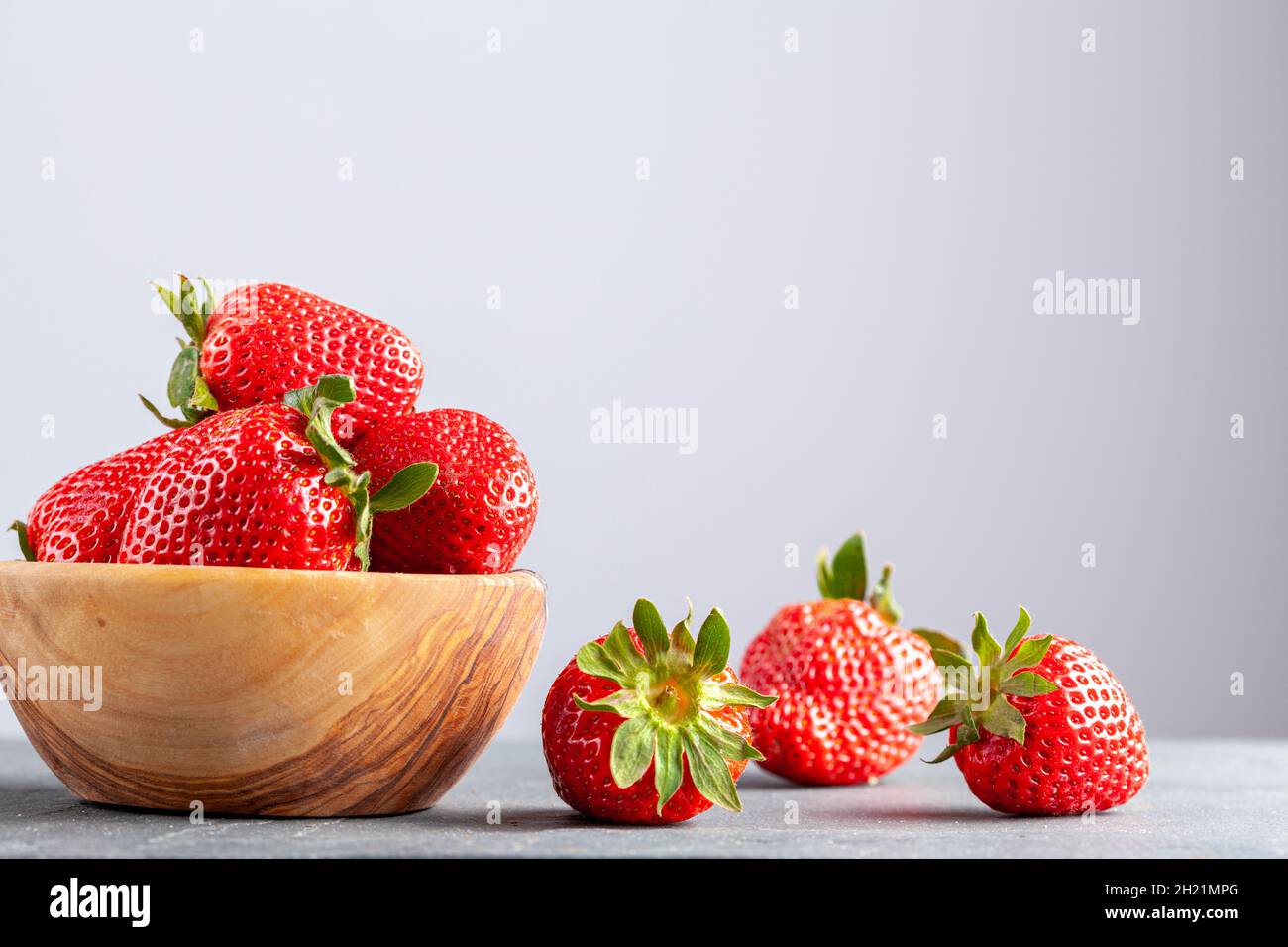 Primo piano immagine isolata di una ciotola di legno riempita con fragole fresche crude su sfondo di pietra scura. Pieno di nutriente, cibo organico crudo per lui Foto Stock